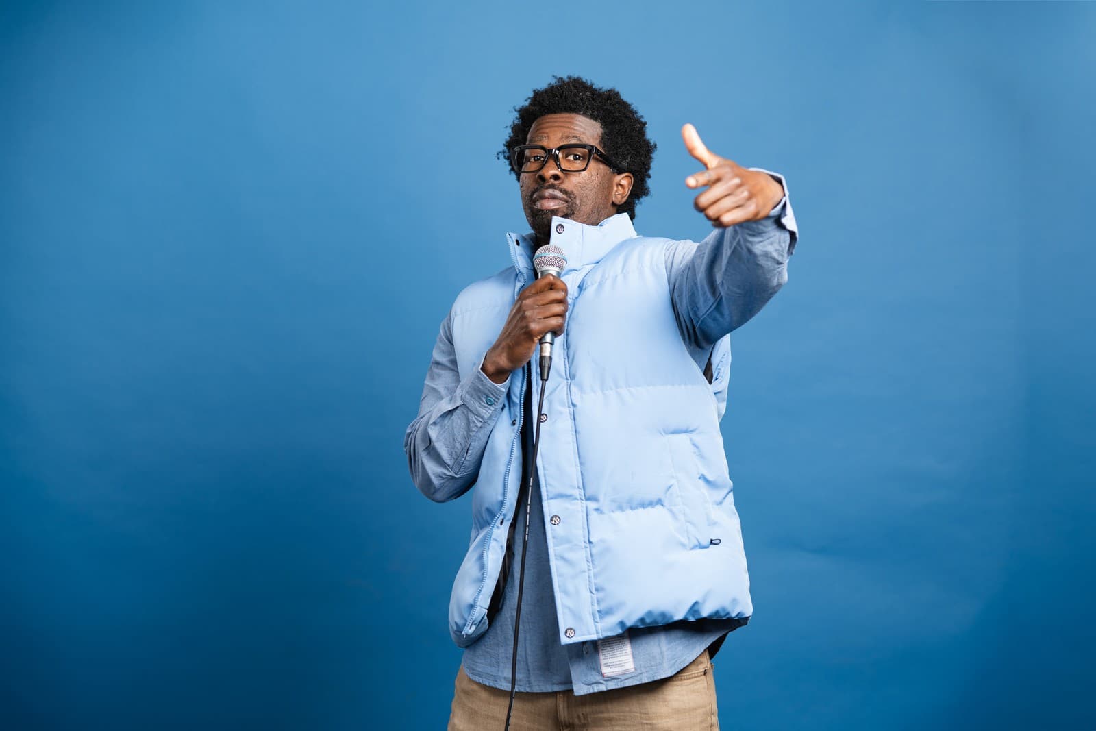 Stroy Moyd pointing at the camera with a microphone, in a light blue vest.